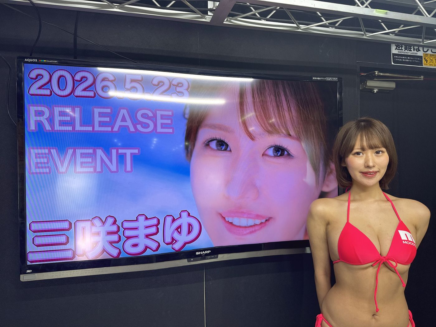 デビューイベントの会場で、告知の画面の横に立つタレント
